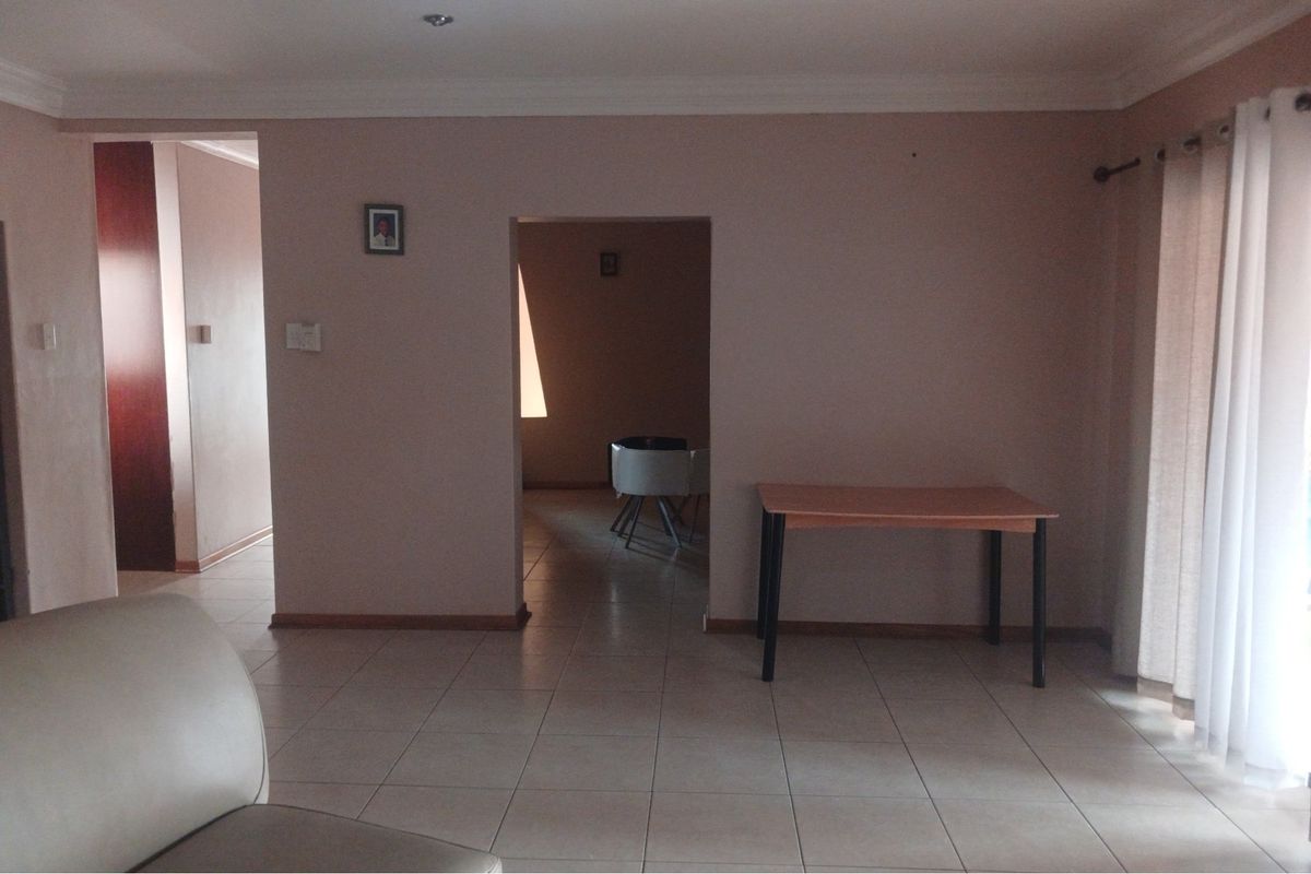 A spacious living area featuring neutral tiled flooring, recessed ceiling lighting, and a doorway leading to an adjacent room.