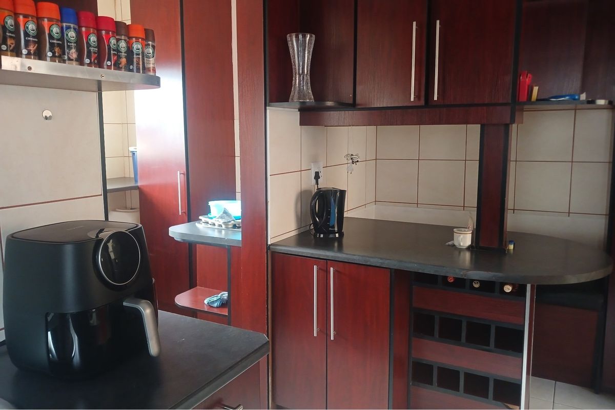 A kitchen featuring dark wood cabinetry, tiled splashbacks, and integrated storage solutions, providing a functional workspace with ample counter area.