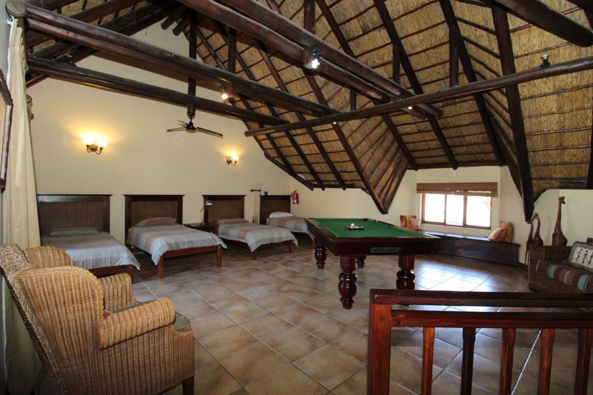 Spacious loft-style bedroom featuring a high vaulted thatched roof with exposed timber beams, tiled flooring, and multiple sleeping areas.