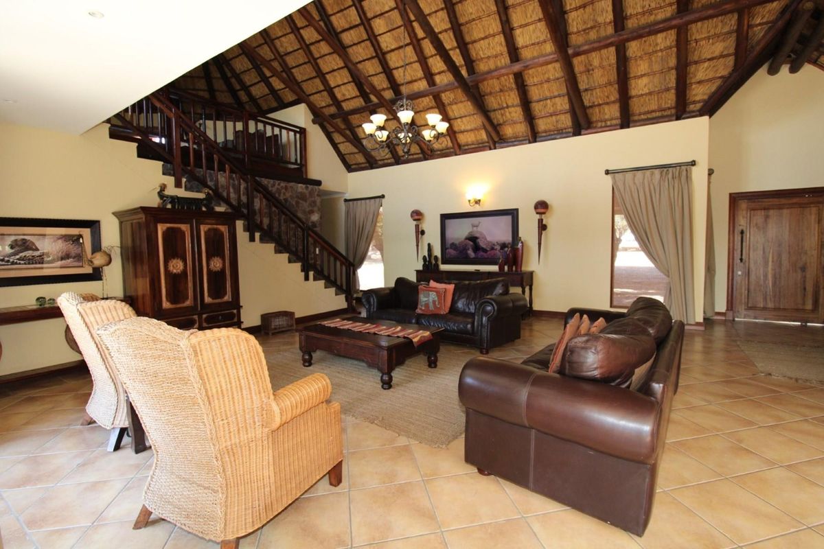 Spacious living room featuring a high vaulted thatched ceiling, exposed timber beams, a mezzanine level with wooden staircase, and tiled flooring.