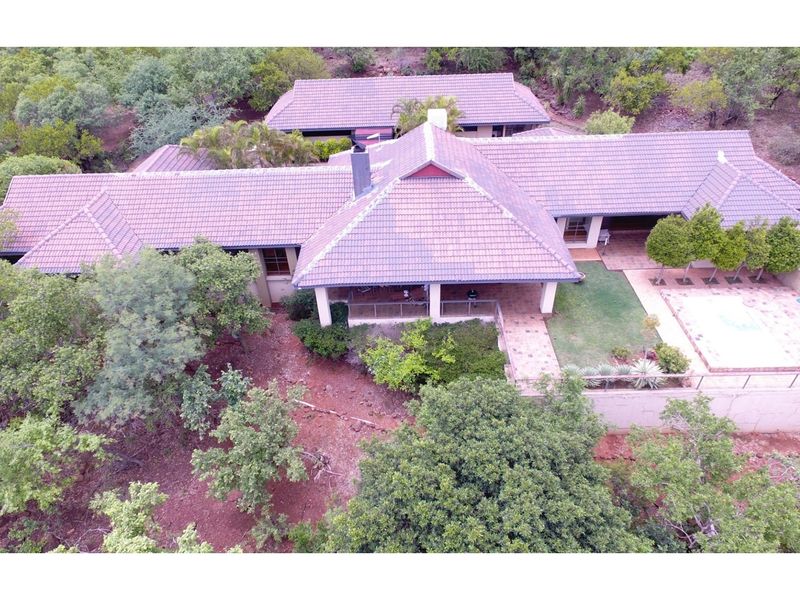 Aerial view of a spacious residential property featuring a tiled roof, covered patio area, swimming pool, and surrounding landscaped garden in a natural setting.