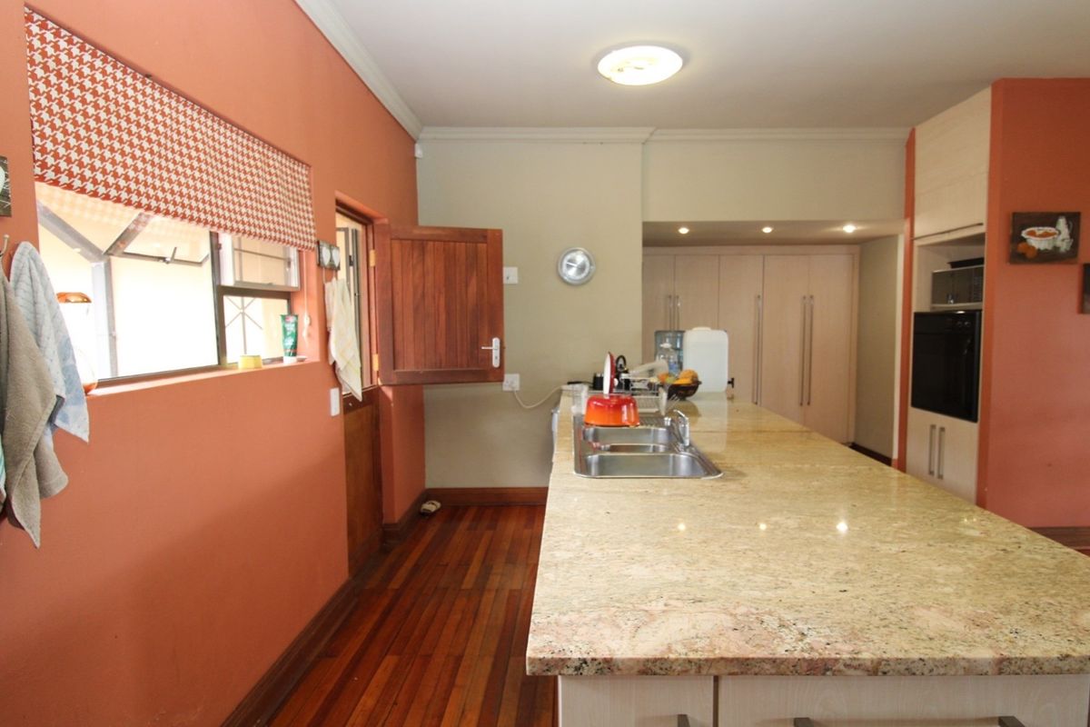 A functional kitchen featuring a large granite-topped island, built-in oven, and warm-toned cabinetry, complemented by rich wooden flooring and a stable-style door.