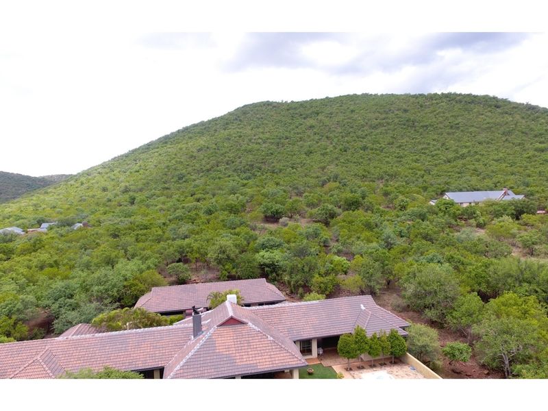 Aerial view of the property featuring a tiled roof structure nestled within a lush, green natural landscape and hilly terrain.
