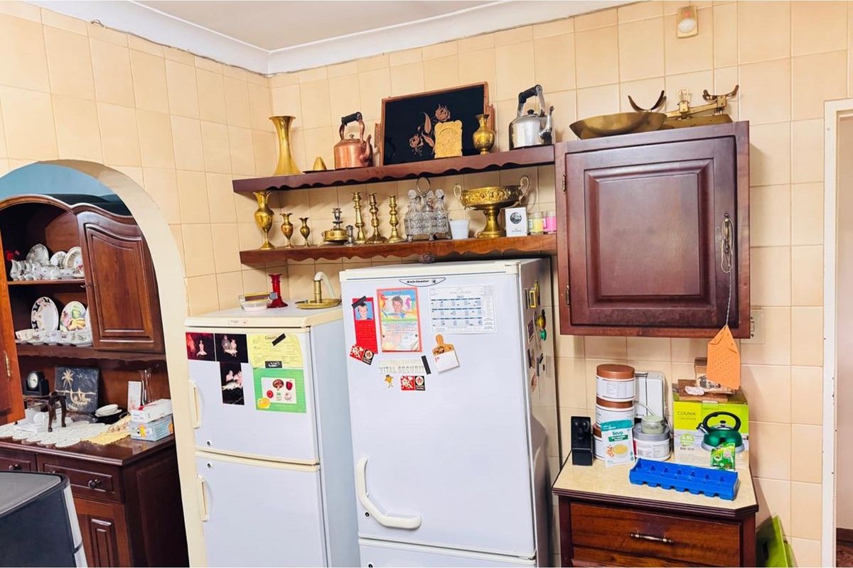 A dated kitchen area featuring traditional wooden cabinetry, wall-mounted shelving, and tiled wall surfaces.