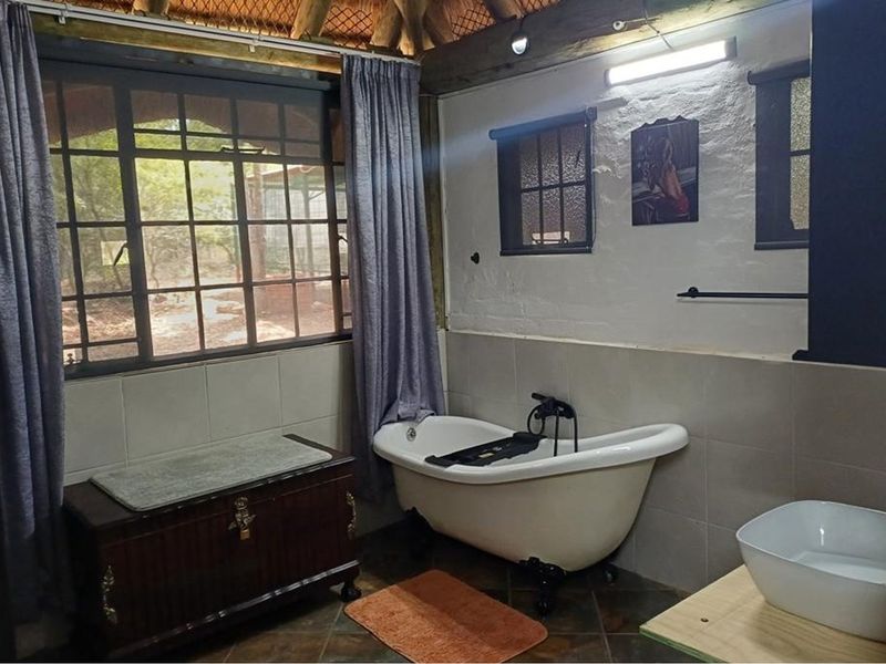 Rustic bathroom featuring a classic freestanding bathtub, vessel sink, and unique thatched ceiling with exposed timber beams, offering a charming, character-filled space.