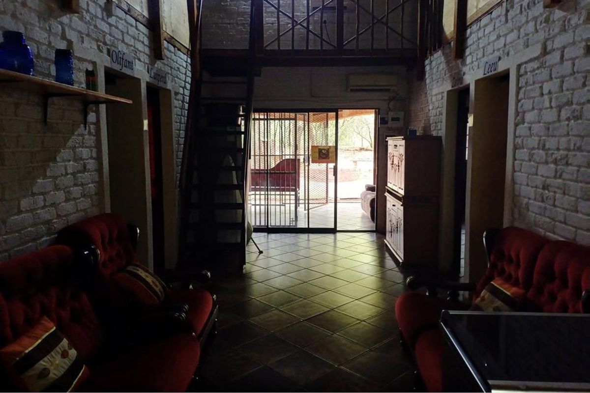 Living area featuring exposed brick walls, tiled flooring, and a mezzanine level with a timber staircase, leading to an outdoor patio area.
