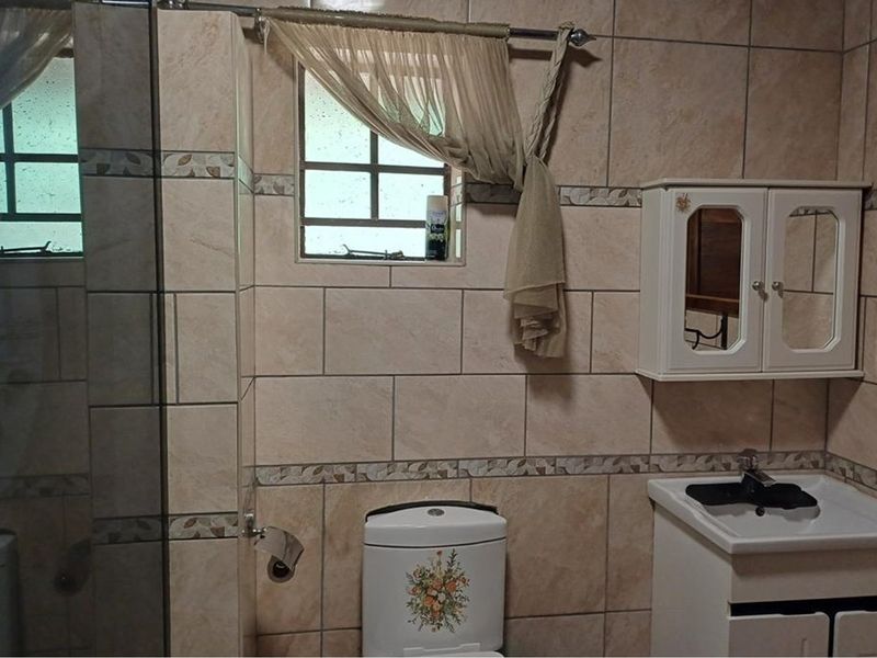 A functional bathroom featuring tiled walls, a vanity cabinet with basin, a toilet, and a shower enclosure.