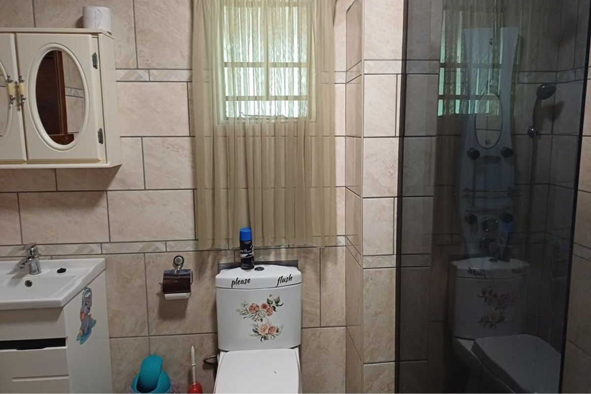 A functional bathroom featuring tiled walls, a wall-mounted vanity, a toilet, and a glass-enclosed shower unit.