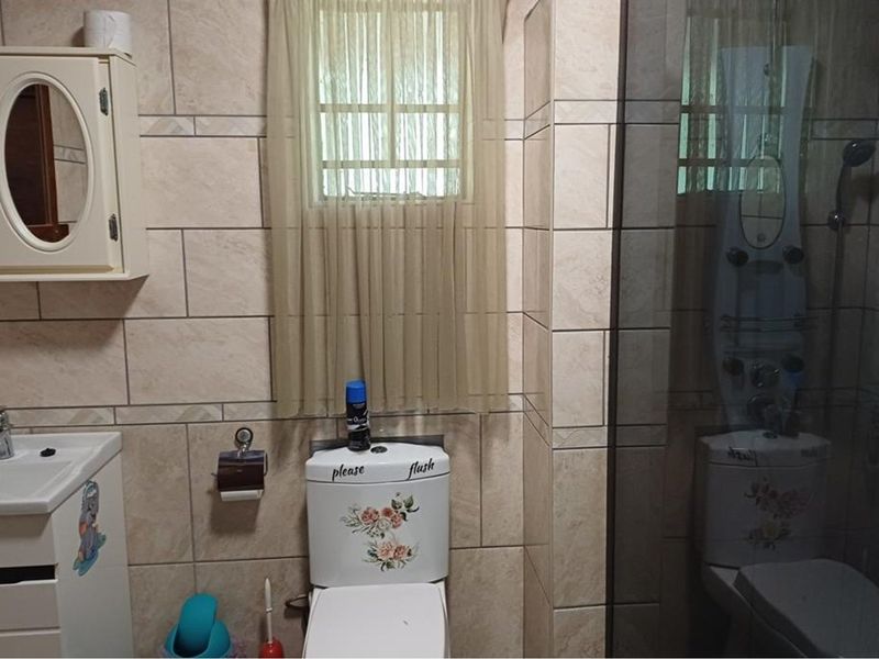 A functional bathroom featuring tiled walls, a wall-mounted vanity, a toilet, and a glass-enclosed shower unit.