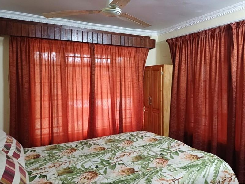 A bedroom featuring a ceiling fan, decorative cornice detailing, and window security bars, offering a functional space with potential for modern updates.