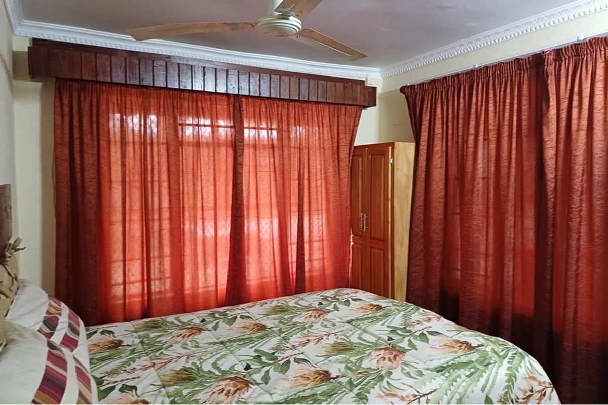 A bedroom featuring a ceiling fan, decorative cornice detailing, and window security bars, offering a functional space with potential for modern updates.