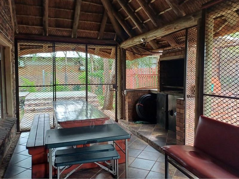 Covered outdoor patio featuring a traditional thatched roof, built-in braai, and tiled flooring, enclosed with security mesh screens for added protection.