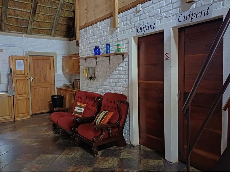 Open plan living area featuring rustic thatched roofing, exposed timber beams, painted brick walls, and slate tile flooring with access to multiple rooms.