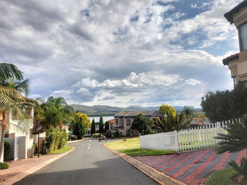 A scenic street view within a residential estate, featuring paved roads, landscaped gardens, and distant mountain and water views.