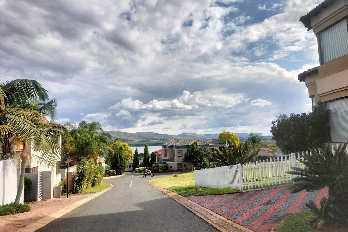 A scenic street view within a residential estate, featuring paved roads, landscaped gardens, and distant mountain and water views.