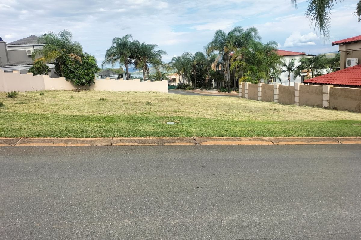 A vacant residential plot featuring a level grassed surface, bordered by established boundary walls and mature palm trees in a residential estate setting.