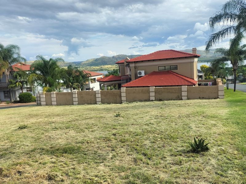 A view of a vacant residential plot with a perimeter wall, overlooking neighboring properties and distant mountain landscape.