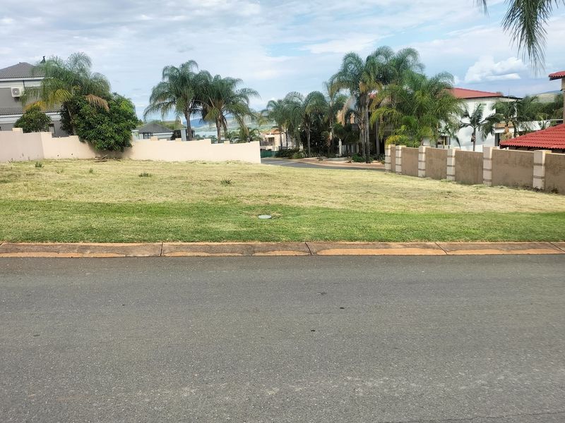 A vacant residential plot featuring a level grassed surface, bordered by established boundary walls and mature palm trees in a residential estate setting.