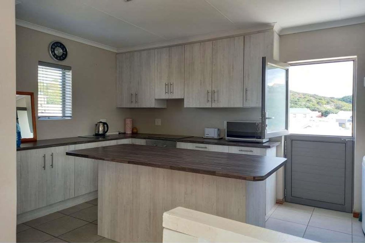 A functional kitchen featuring light wood-grain cabinetry, a dark laminate breakfast bar, tiled flooring, and direct access to an outdoor area.
