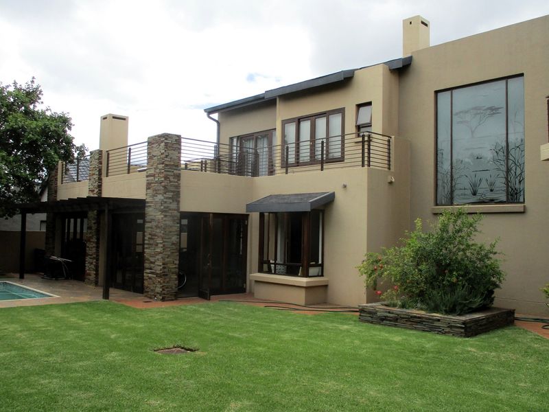 Rear view of a multi-story house featuring a swimming pool, landscaped garden, stone-clad pillars, and a spacious upper-level balcony with metal railings.