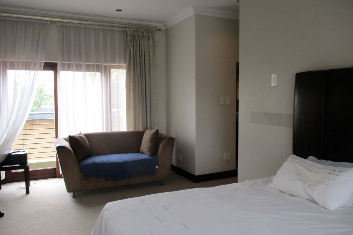A spacious bedroom featuring neutral carpeting, recessed ceiling lighting, and a sliding glass door providing access to an outdoor balcony area.
