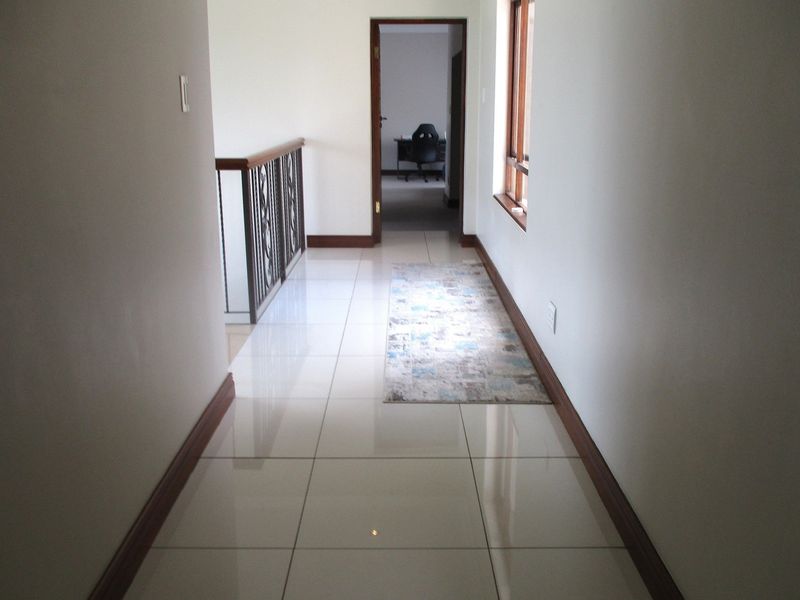 A bright, tiled hallway featuring a decorative metal balustrade and wooden skirting boards, leading towards an adjacent room.