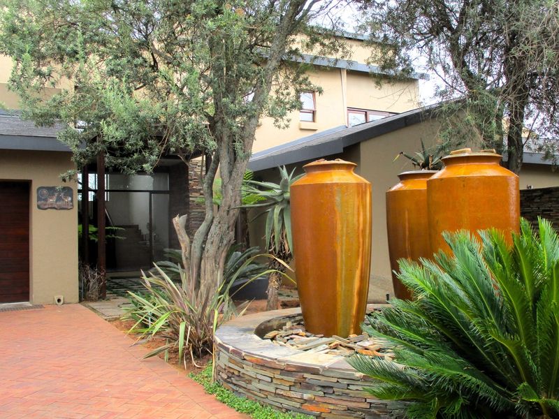 A modern front entrance featuring a brick driveway, stone-clad water feature, and a dark wood garage door set against a contemporary architectural facade.