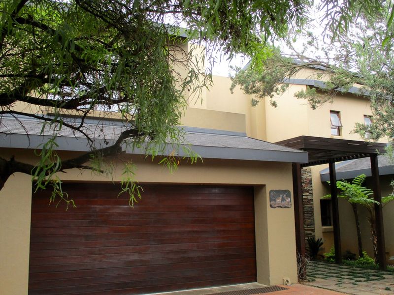 Front elevation of a modern house featuring a double garage with a wooden door, stone cladding accents, and a covered entrance walkway.