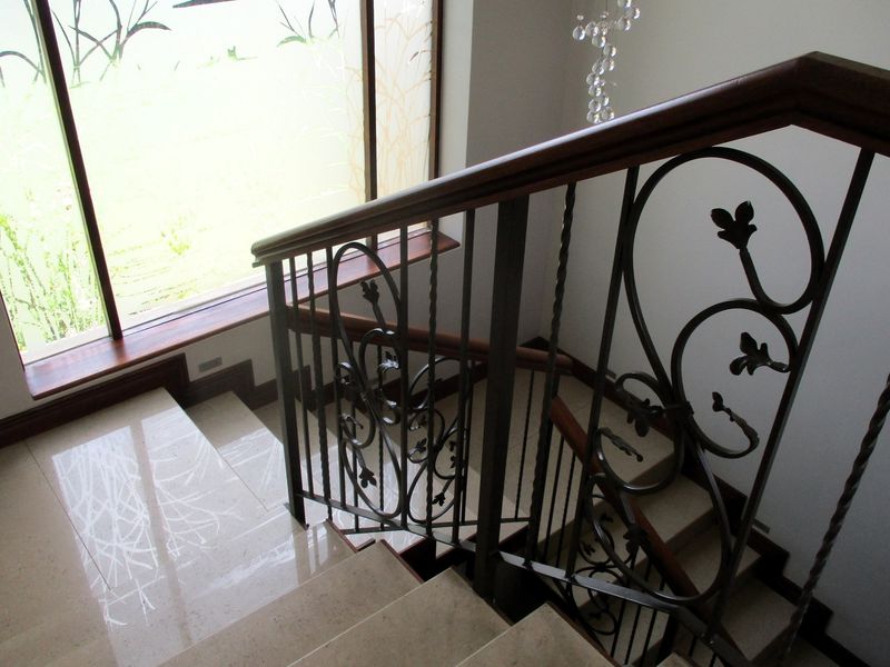 A staircase featuring polished stone treads, a decorative wrought iron balustrade with a wooden handrail, and a large window with frosted glass detailing.
