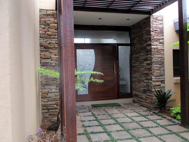 A welcoming front entrance featuring a solid timber door with decorative glass inlay, framed by natural stone cladding and a timber pergola structure.
