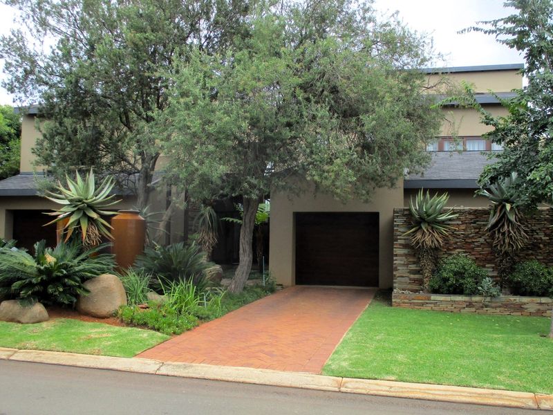 Front elevation of a modern house featuring a paved driveway, integrated garage, and established landscaped garden with stone feature wall.