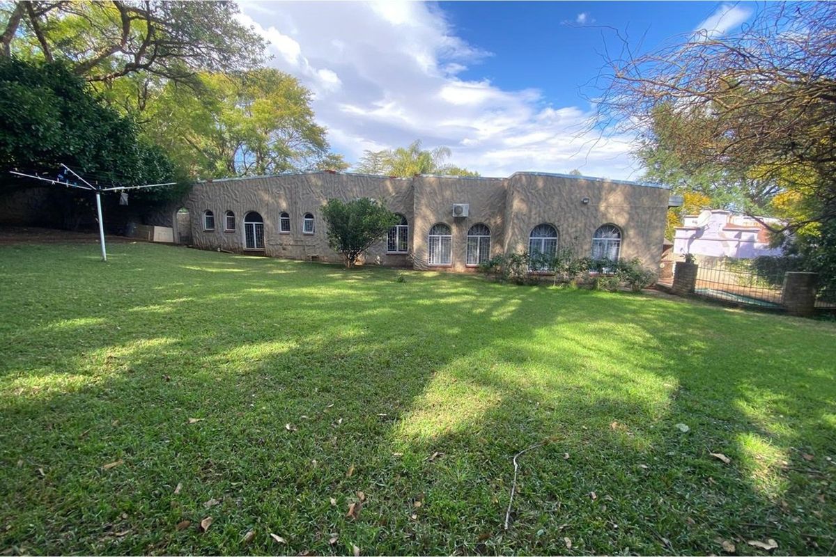 Rear view of the property featuring a large lawn, textured exterior walls, and multiple arched windows with security bars.