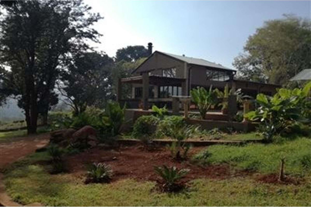 A view of the farm property featuring a multi-level dwelling with a covered patio area, surrounded by established trees and landscaped garden grounds.