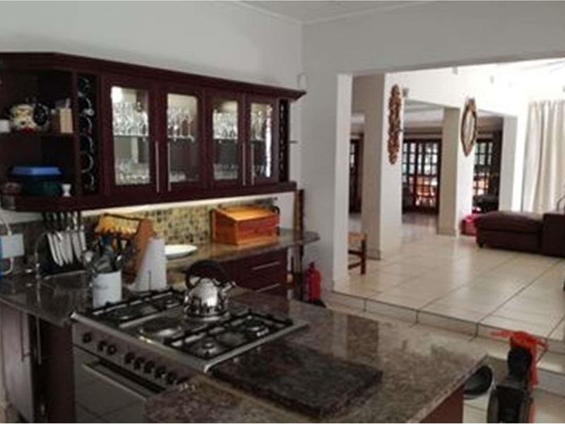 A kitchen featuring dark wood cabinetry, granite countertops, and a built-in gas hob, opening into an adjacent living area with tiled flooring.