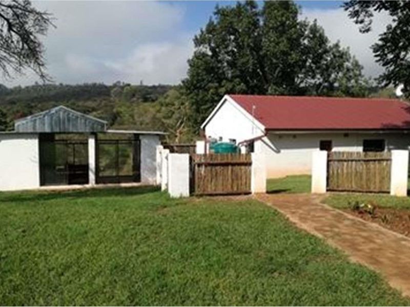 A view of the farm property featuring a main dwelling with a red roof, a secondary structure, and a paved walkway through the garden.