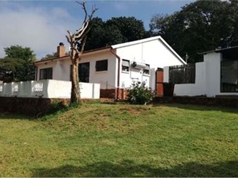 Rear view of the farm dwelling featuring a white rendered facade, a raised patio area, and a spacious surrounding lawn.