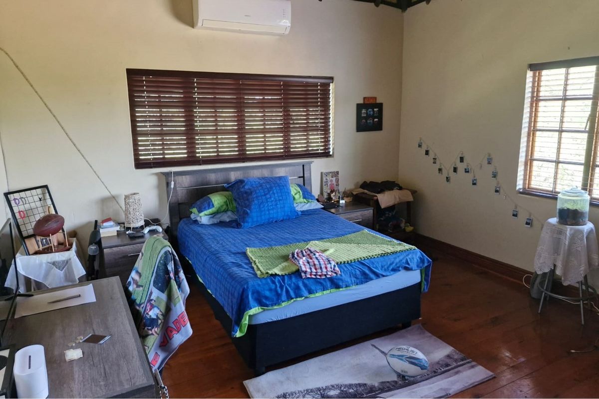 A bedroom featuring timber flooring, timber venetian blinds, and a wall-mounted split-system air conditioning unit.