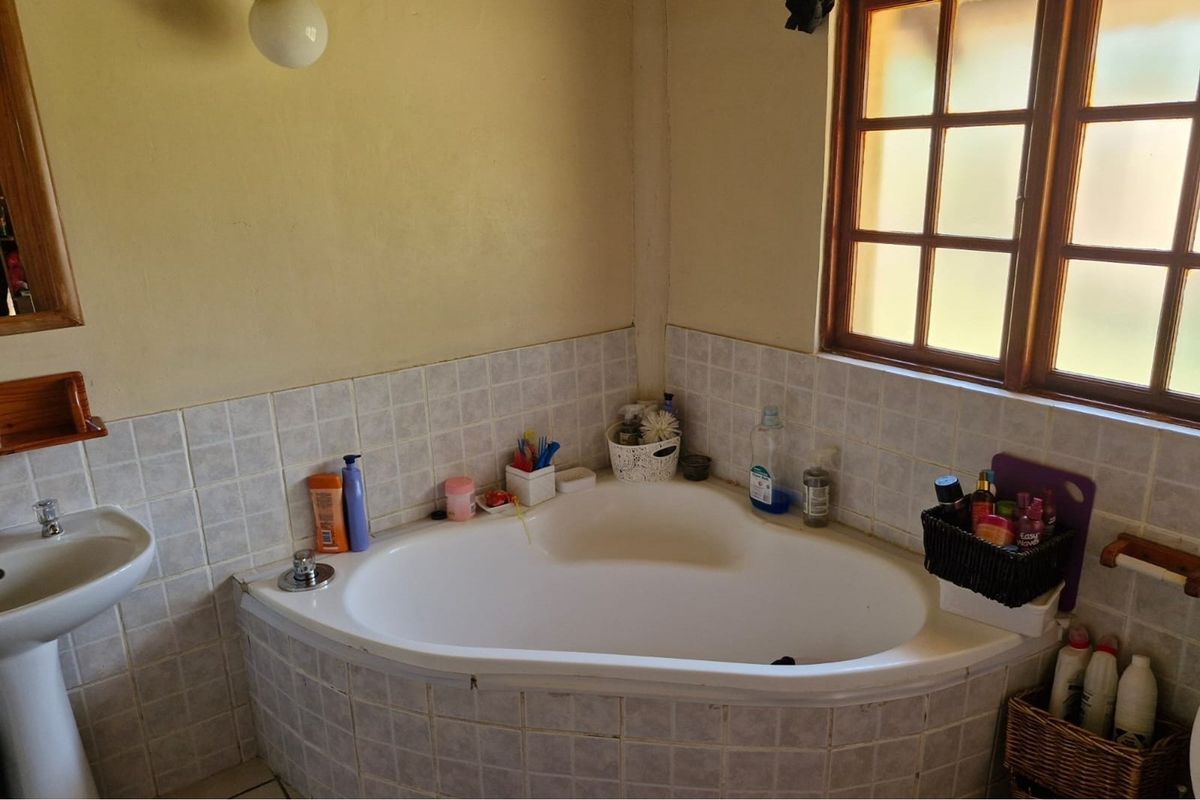 A functional bathroom featuring a corner bathtub, pedestal basin, and tiled splashback, illuminated by a timber-framed window.