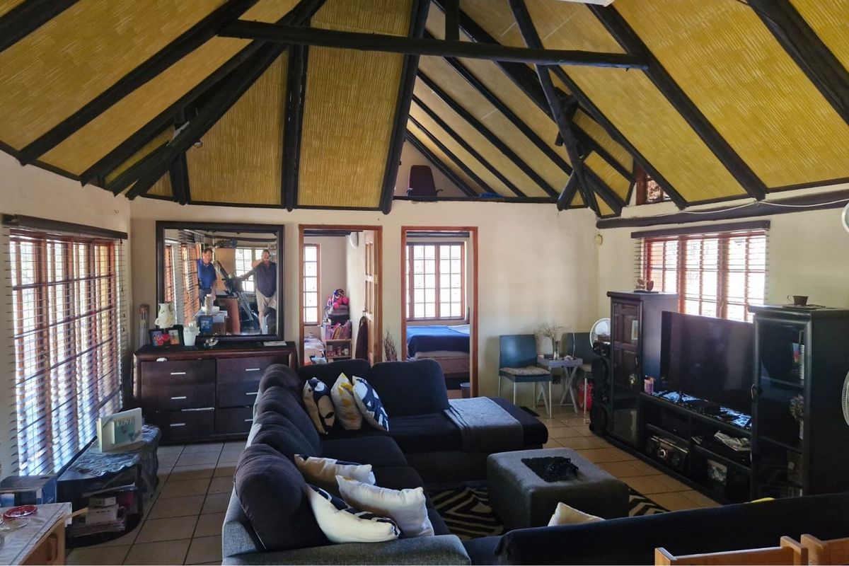 Spacious living room featuring a high vaulted ceiling with exposed timber beams, tiled flooring, and large timber-framed windows allowing for natural light.
