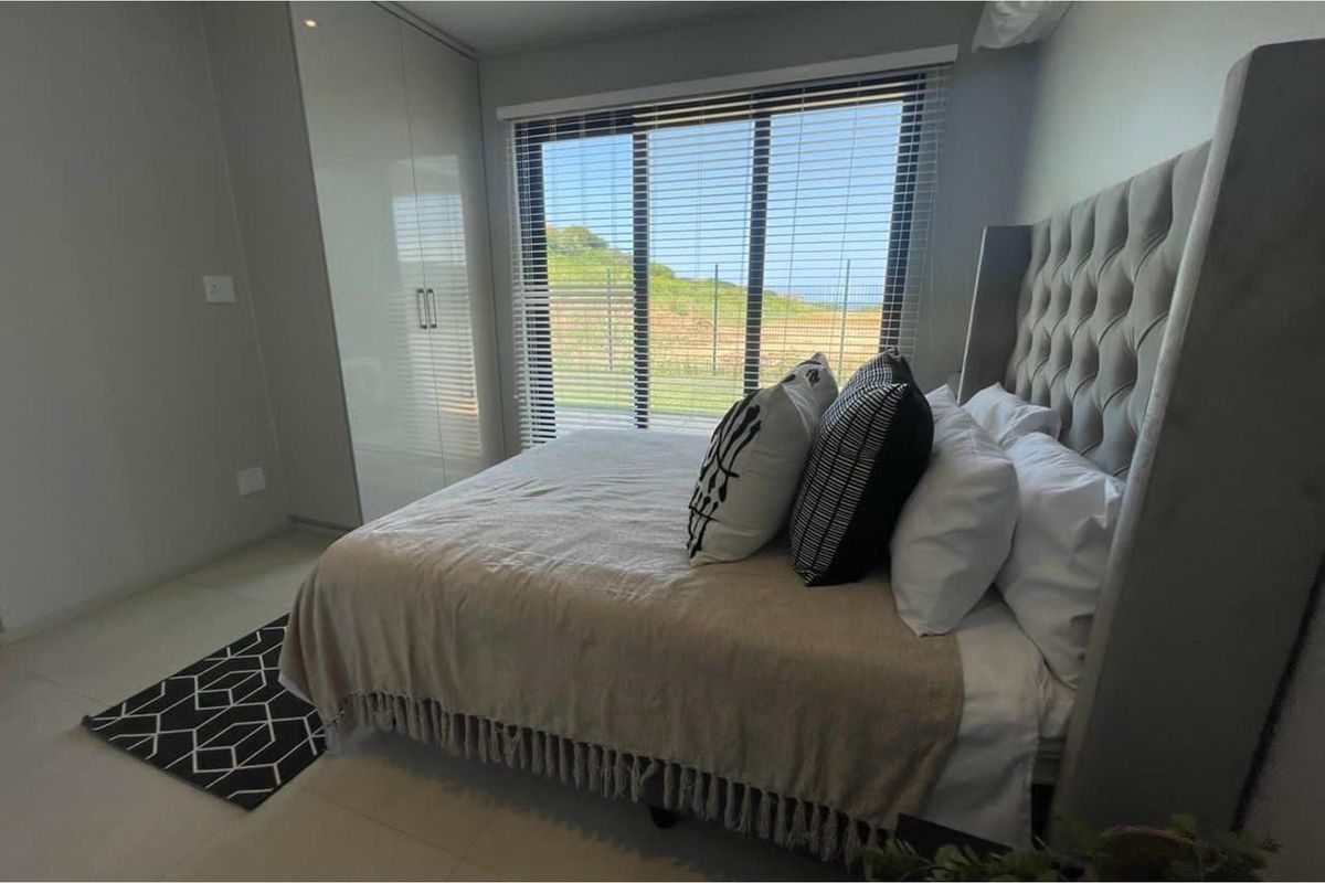A modern bedroom featuring built-in floor-to-ceiling wardrobes, tiled flooring, and large windows with fitted blinds offering natural light.