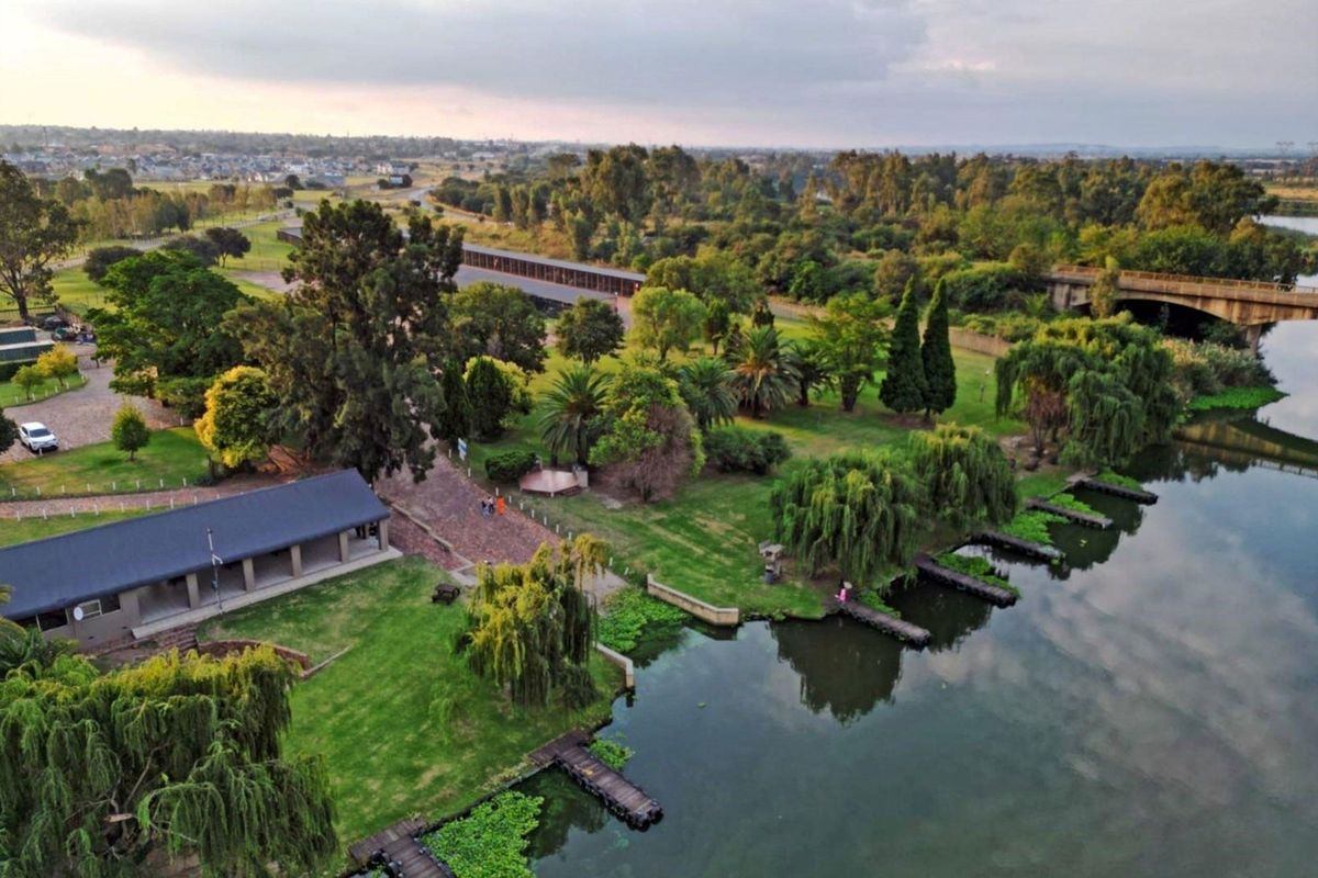 Aerial view of a riverside property featuring landscaped gardens, a covered patio area, and private wooden jetties along the water's edge.