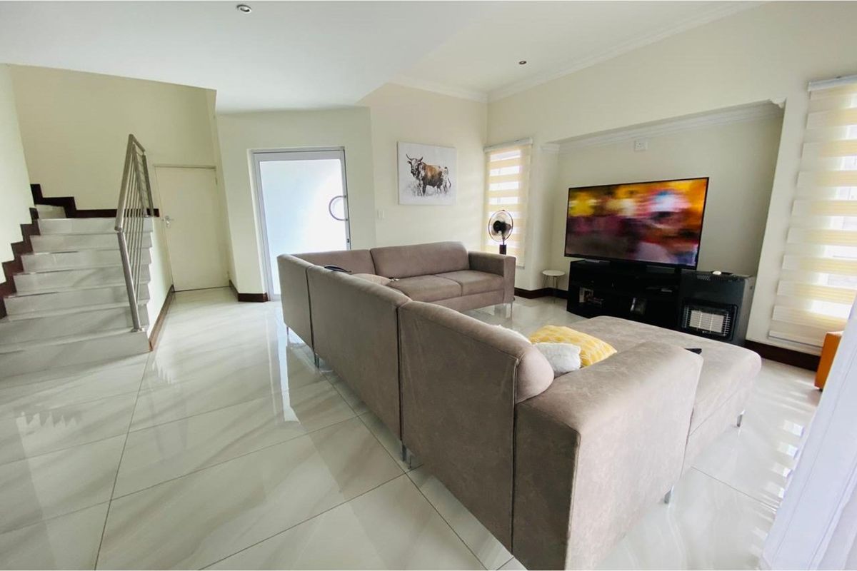 A bright living room featuring polished porcelain floor tiles, a staircase with a stainless steel balustrade, and modern recessed ceiling lighting.