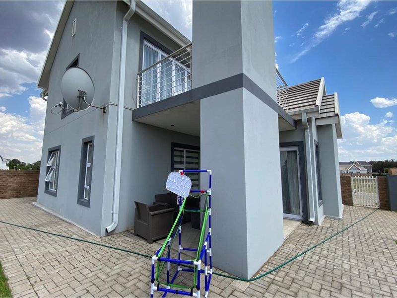 Rear view of a modern two-story house featuring a paved patio area, a balcony with stainless steel railings, and a chimney stack.