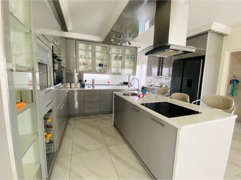 Modern kitchen featuring high-gloss grey cabinetry, a central island with a built-in induction hob, stone countertops, and integrated stainless steel appliances.