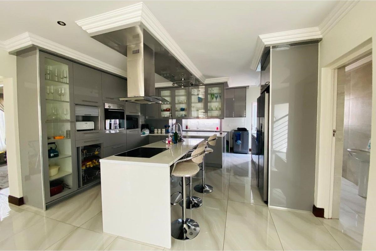 Modern kitchen featuring high-gloss grey cabinetry, a central island with a built-in cooktop, stainless steel extractor fan, and polished porcelain floor tiles.