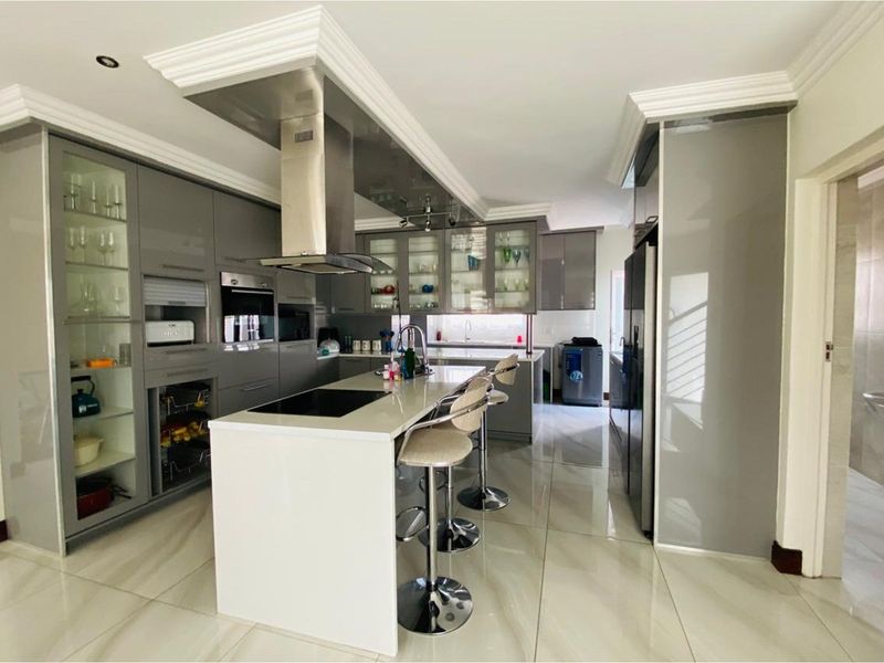 Modern kitchen featuring high-gloss grey cabinetry, a central island with a built-in cooktop, stainless steel extractor fan, and polished porcelain floor tiles.