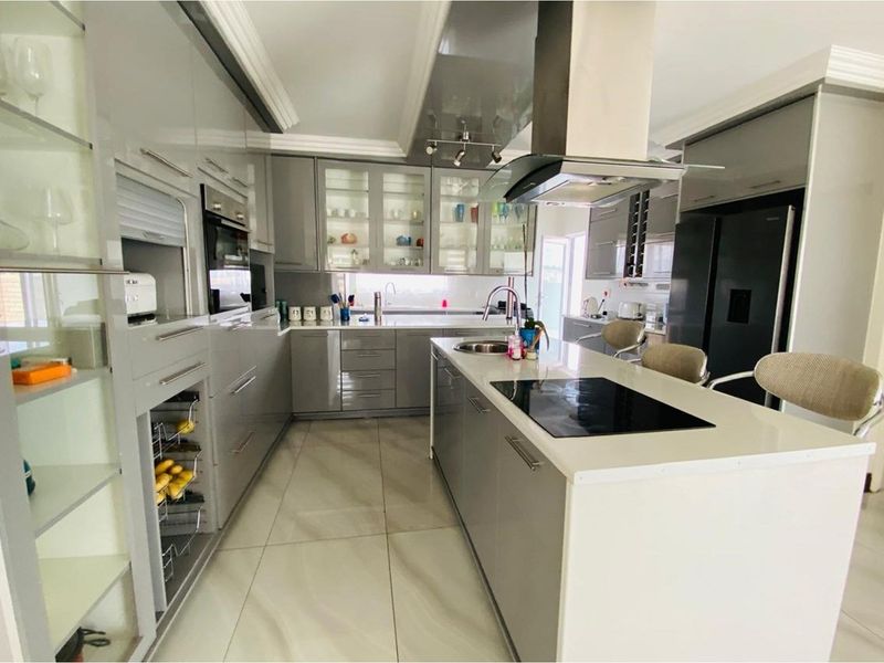Modern kitchen featuring high-gloss cabinetry, a central island with a built-in induction hob, stone countertops, and integrated stainless steel extractor fan.