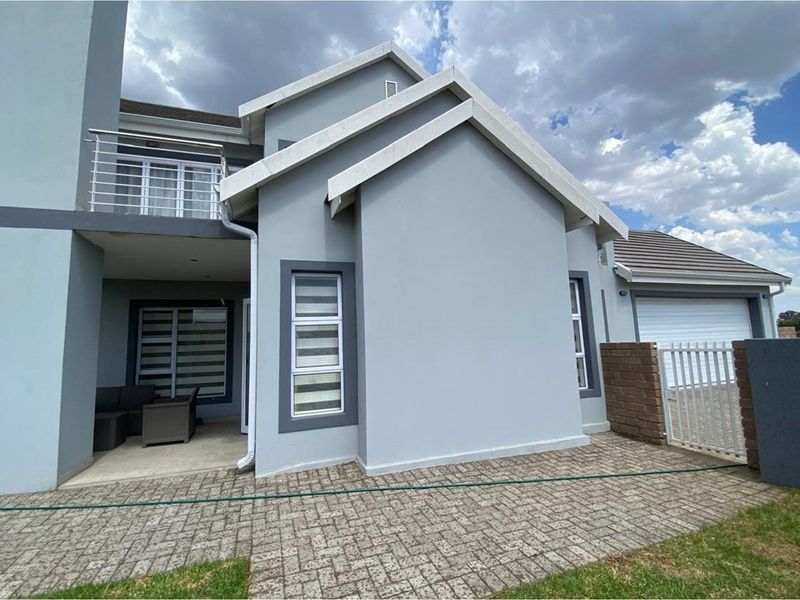 A modern exterior view of the house featuring a paved driveway, covered patio area, balcony with stainless steel railing, and a garage.