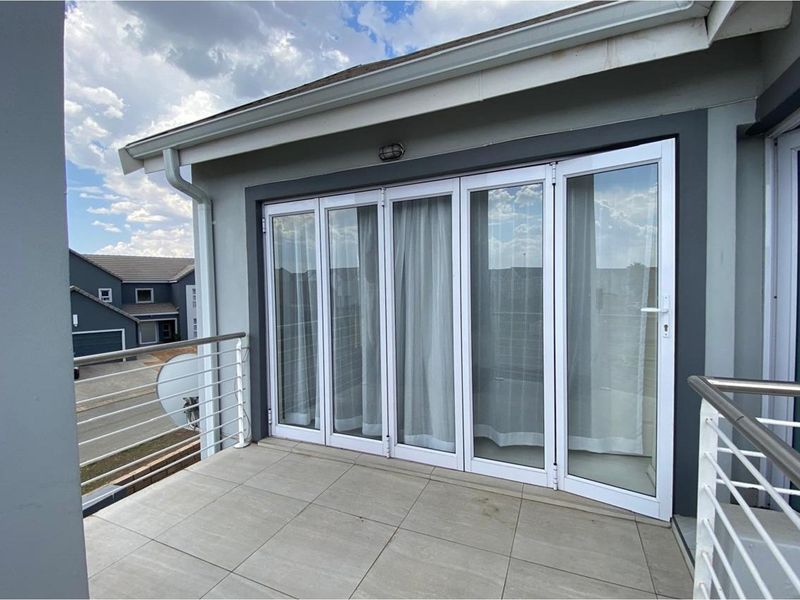 A modern balcony featuring tiled flooring, stainless steel railings, and white framed folding glass doors providing seamless indoor-outdoor access.