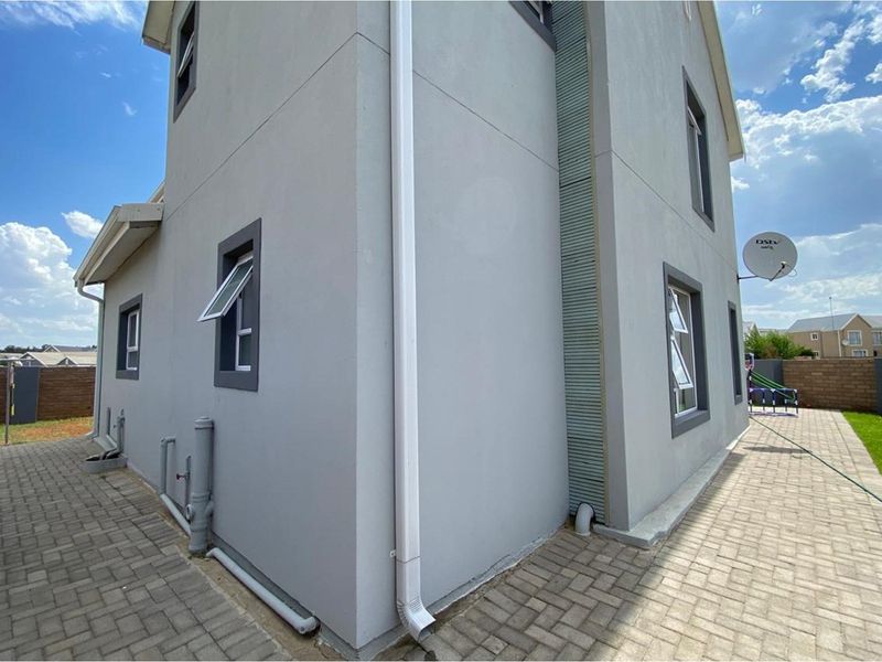 Side and rear exterior view of the double-story house featuring paved walkways, downpipes, and a satellite dish.